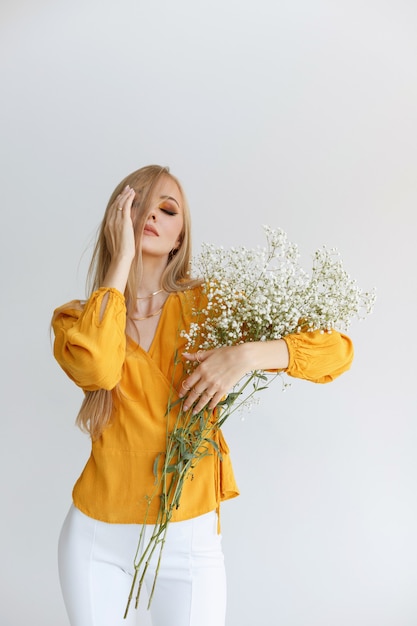 Model in een gele blouse met delicate bloemen op een grijze achtergrond met herfstmake-up