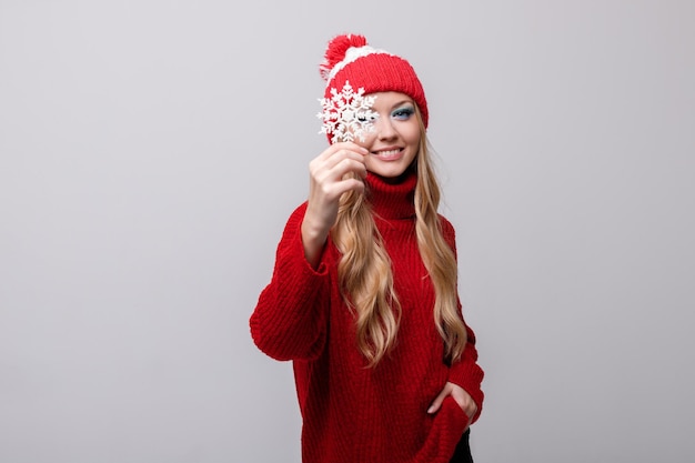 Model in een rode trui en muts met een sneeuwvlok op een grijze achtergrond