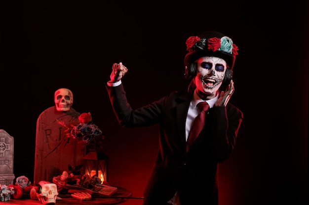 Model in halloween kostuum luisteren naar lied in studio, staande op zwarte achtergrond. Het dragen van la cavalera catrina make-up en het vieren van dios de los muertos Mexicaanse vakantie met audio-headset.