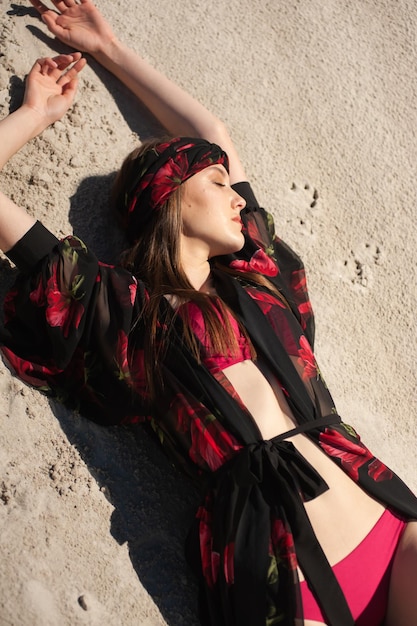 A model is laying in the sand and wearing a red outfit with a black belt.