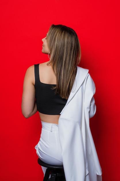 the model is sitting on a chair with her back to the camera in a stylish white suit on a red background