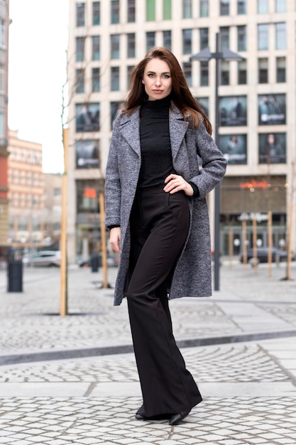 The model is a stylish woman in full height walking in the square, dressed in a warm coat, trousers and a jumper in the style of street fashion.