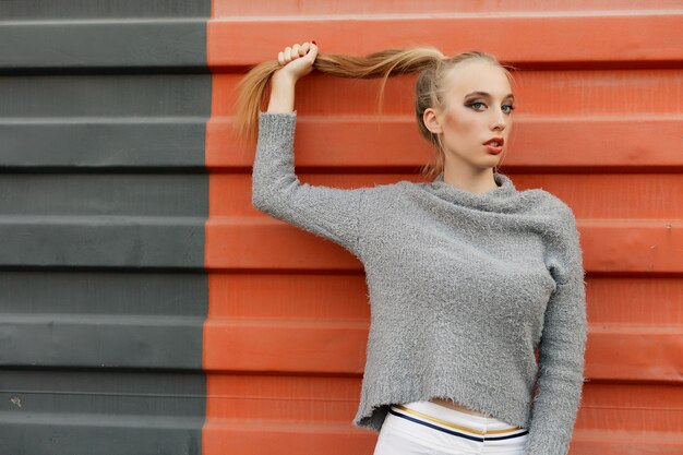 Model pointing upwards in studio and looking at camera. isolated orange background. Smiling woman in sweater posing with crossed arms and looking at the camera over yellow background