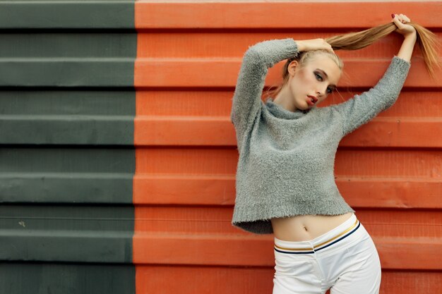 Model pointing upwards in studio and looking at camera. isolated orange background. Smiling woman in sweater posing with crossed arms and looking at the camera over yellow background