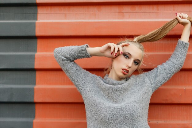 Model pointing upwards in studio and looking at camera. isolated orange background. Smiling woman in sweater posing with crossed arms and looking at the camera over yellow background