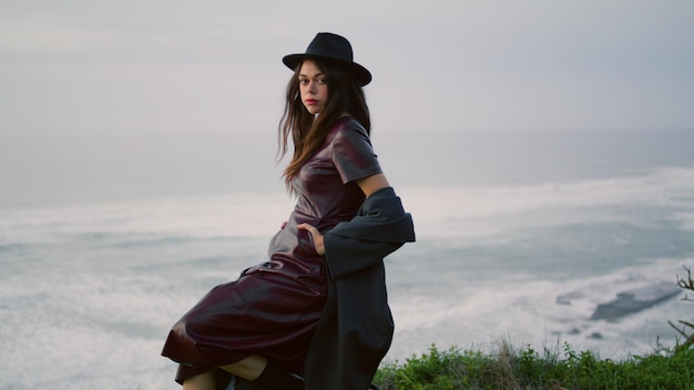 Model posing nature twilight wearing stylish hat woman sitting at stormy sea