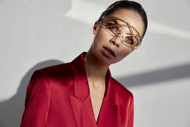 model in a red jacket on a light background looks ahead and jewelry on her face High quality photo