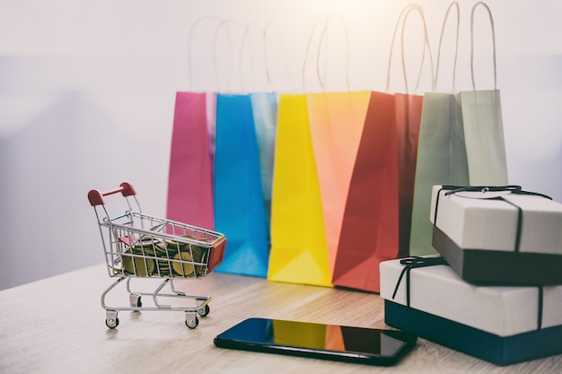 Model of Shopping Cart on wooden floor and gift box, shopping bag and smartphone