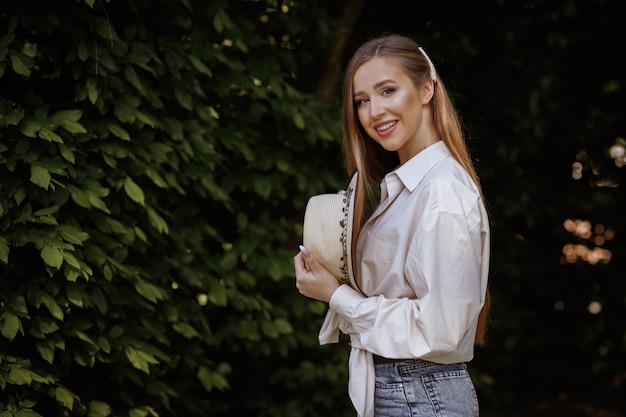 Model smiling on a green space with a straw hat. summer walk in the park