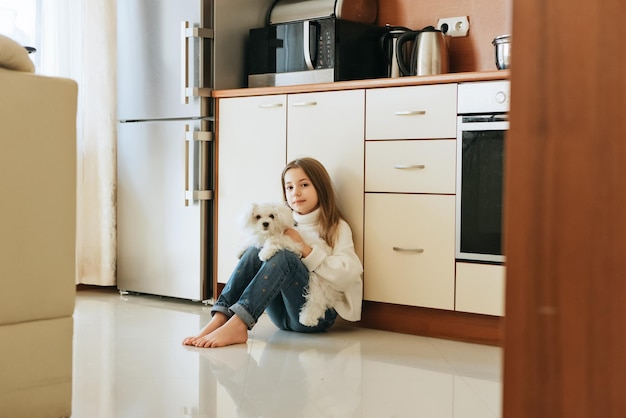 model speelt met huisdier witte hond Maltese schoolmeisje thuis levensstijl in beige keuken