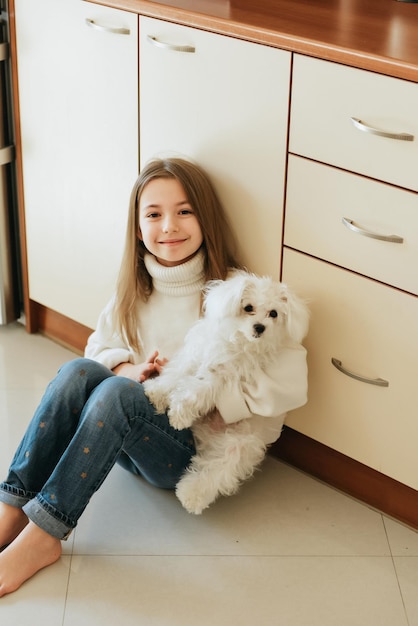 model speelt met huisdier witte hond Maltese schoolmeisje thuis levensstijl in beige keuken