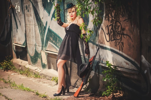 Model standing in front of stone wall with graffiti near gun