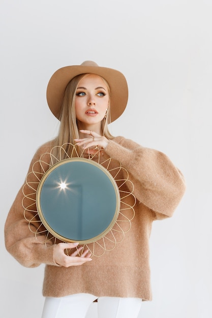 Model in stylish autumn clothes with makeup with a mirror on a gray background. Creative