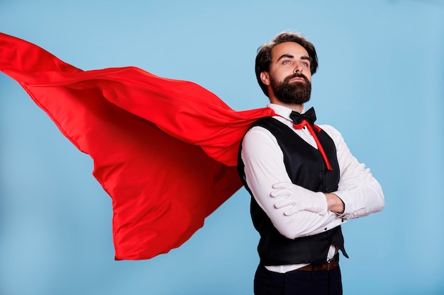 Photo model superhero with cartoon cape posing over blue background, wearing fantasy leader costume with suit and tie in studio. young adult acting powerful to protect people, strong superhuman.