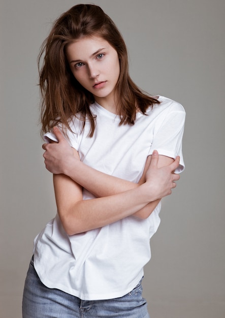 Model test portrait with young beautiful fashion model posing on grey background. Wearing white t-shirt and jeans.