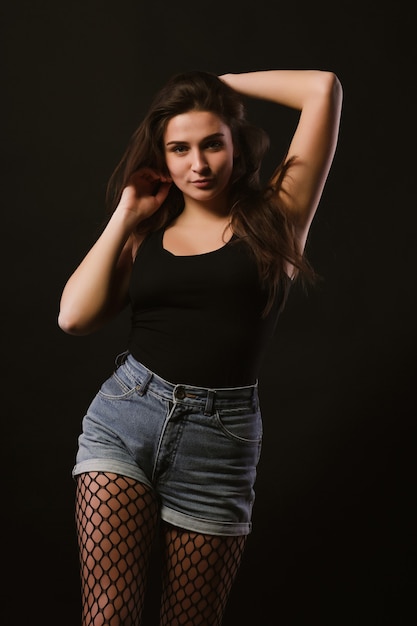 Model test with adorable brunette woman in black shirt and jeans shorts posing in the shadows