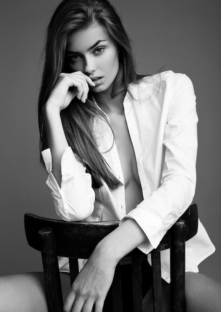 Model test with young beautiful fashion model wearing white shirt sitting on chair 