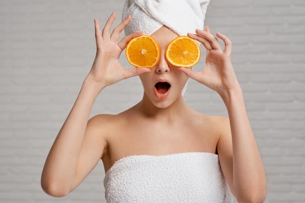 Model in towels holding two pieces of orange closing eyes