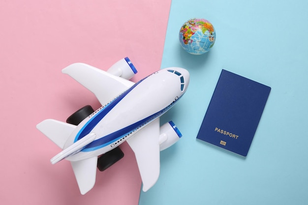 Model of toy passenger plane passport and globe on bluepink pastel background Travel concept Top view