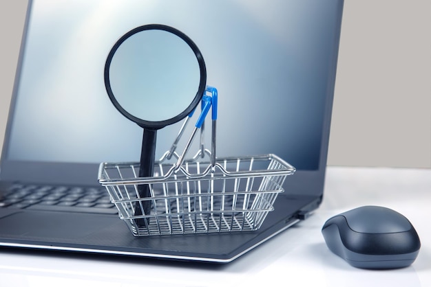 Model van een boodschappenwagentje en een vergrootglas op de achtergrond van een laptop Product zoeken online shopping websites