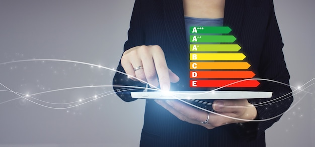 Foto model van energie-efficiëntie. witte tablet in zakenvrouw hand met digitale hologram energie-efficiëntie pictogram teken op grijze achtergrond. energie-efficiëntieconcept.