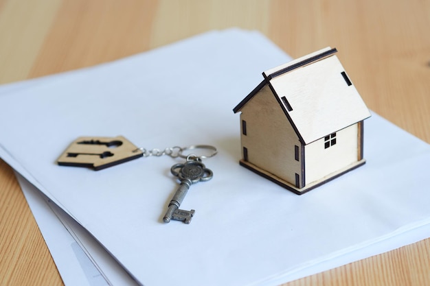 Model van het huis een metalen sleutel met een sleutelhanger een contract op een houten tafel