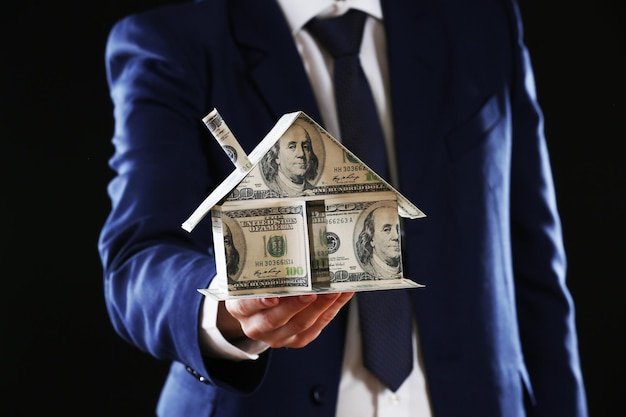 Model van huis gemaakt van geld in mannelijke handen op donkere achtergrond