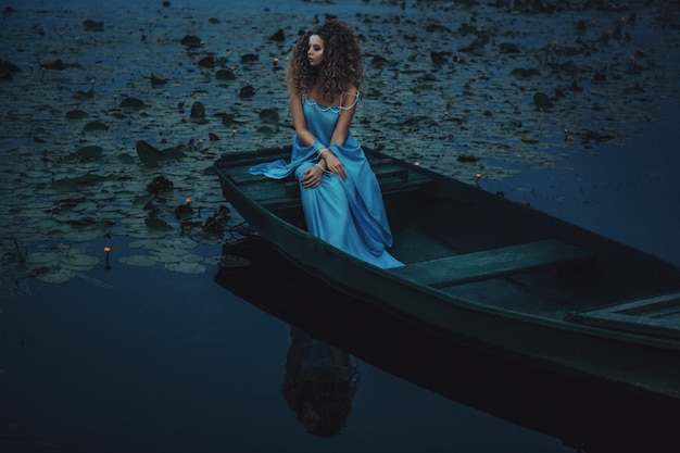 Model wearing blue dress is posing in a boat on the water