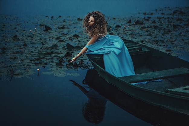 青いドレスを着ているモデルは水にボートでポーズをとってください。