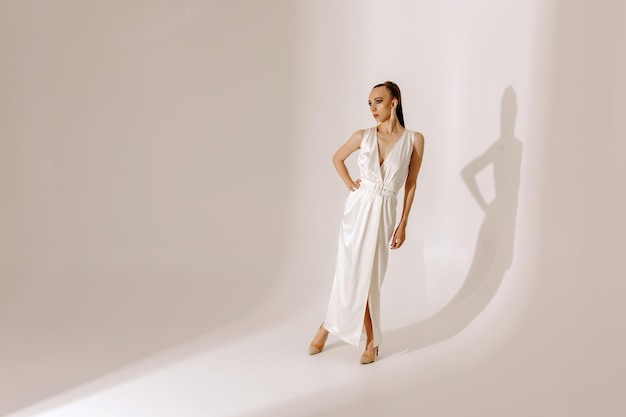 A model in a white dress stands in front of a white backdrop.