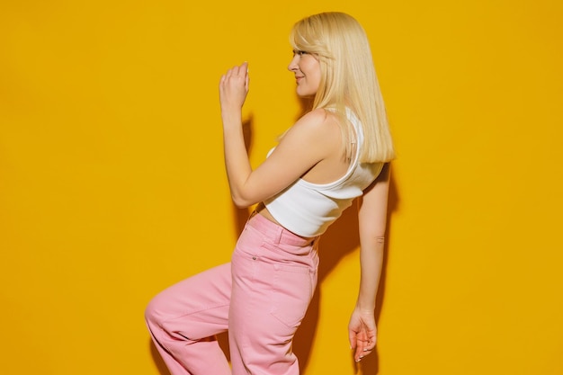 A model in a white top and pink jeans poses on a yellow background A young woman in stylish clothes is fooling around in front of the camera