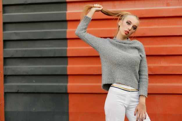 Model wijst naar boven in de studio en kijkt naar de camera. geïsoleerde oranje achtergrond. Glimlachende vrouw in trui poseren met gekruiste armen en kijken naar de camera over gele achtergrond