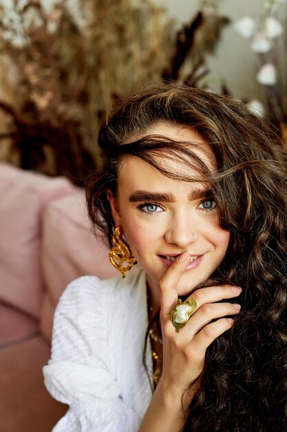 Model with beautiful eyes curly hair and thick eyebrows Smiles finger near lips Fashion and style