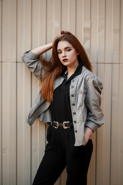 Model woman in a fashionable jacket and black polo shirt posing near a metal container on the street