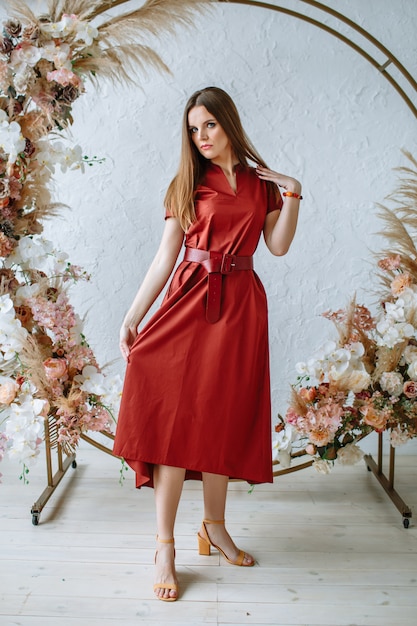 Model woman in a red dress on the background of a flower arch