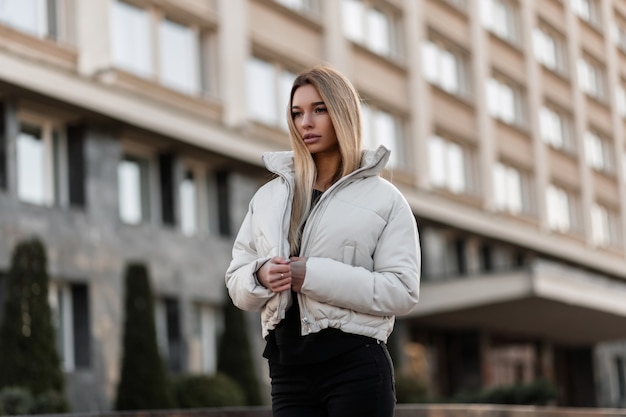 model of a young woman in a white jacket and a leather trendy bag stands in the city