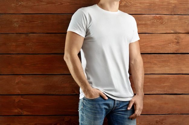 Modelkleding. Gespierde slanke man in een wit T-shirt en spijkerbroek op een bruine houten studioachtergrond. Sjabloon klaar voor u showcase.