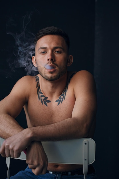 Modelling snapshots pensive frustrated tanned attractive\
handsome naked man sit on chair smoking looks at camera posing\
isolated in black studio background fashion offer copy space for ad\
closeup