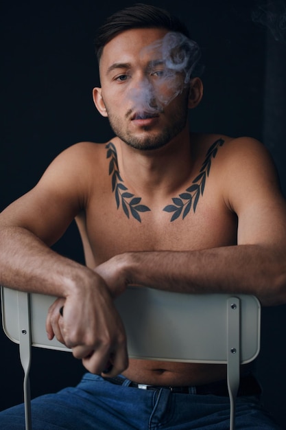 Modelling snapshots pensive frustrated tanned attractive\
handsome naked man sit on chair smoking looks at camera posing\
isolated in black studio background fashion offer copy space for ad\
closeup