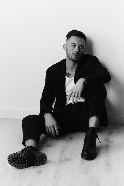 Modelling snapshots serious selfconfident attractive handsome\
man in black jacket sitting on floor posing in white studio\
background black and white concept copy space