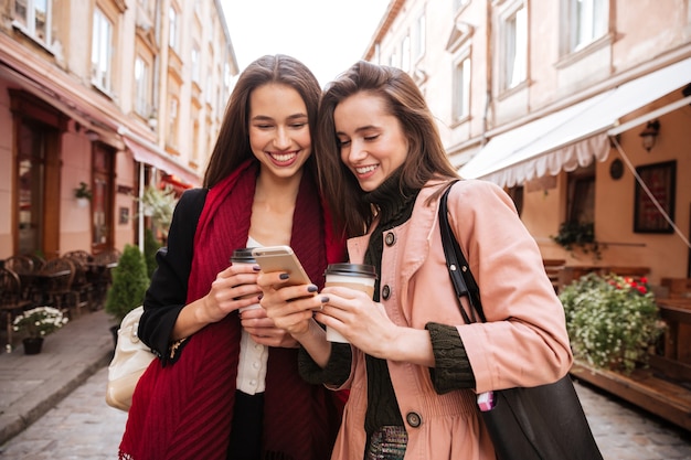 Models in coats looking at phone. on the street