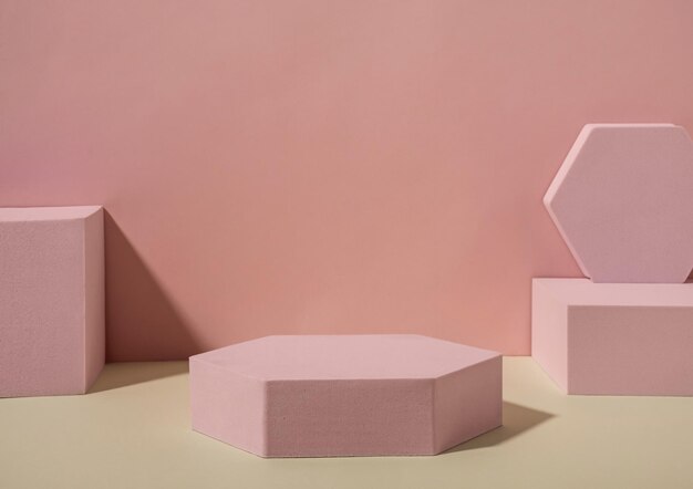 Models of pink geometrical shapes, squares and hexagons, placed on sandy floor against the wall with shadows. Copy space concept