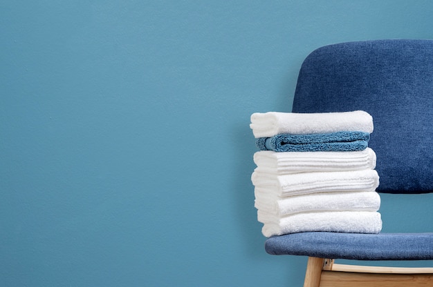 Modelstapel schone handdoeken op houten stoel met blauwe muurachtergrond, exemplaarruimte.