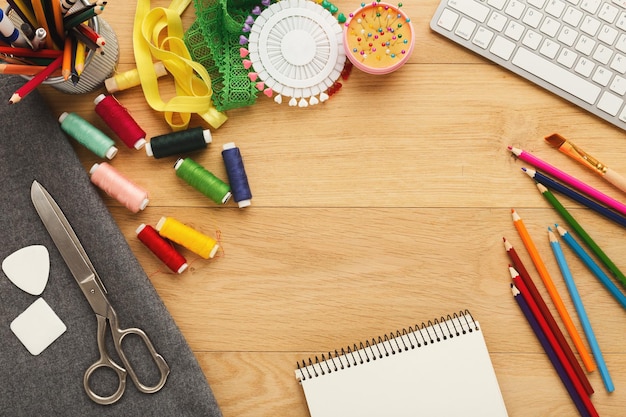 Modeontwerper werkruimte bovenaanzicht. Naaiuitrusting, kleurpotloden, laptop en notitieblok op houten tafel met kopieerruimte