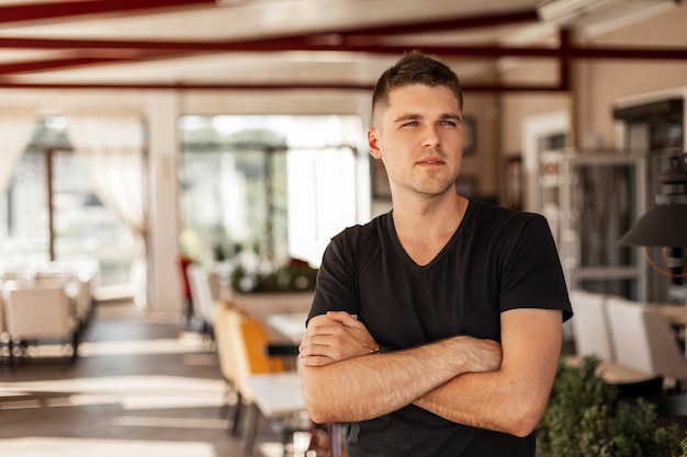 modern american man model of a young man with a stylish hairstyle in a fashionable black t-shirt posing standing in vintage cafe