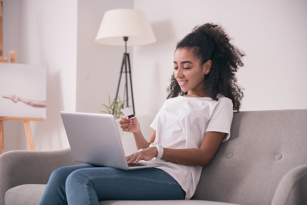 Modern apparaat. Aangename jonge vrouw die haar laptop vasthoudt terwijl ze een online betaling doet