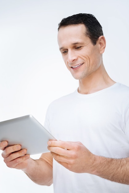 Modern apparaat. Gelukkig vrolijke aardige man glimlachend en kijken naar het tabletscherm tijdens het surfen op internet