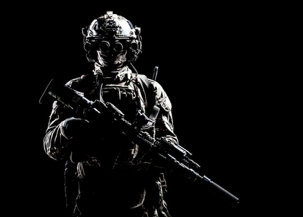 Modern army special forces equipped soldier, anti terrorist squad fighter, elite mercenary armed assault rifle, standing in darkness with night vision goggles on helmet, studio portrait, copyspace