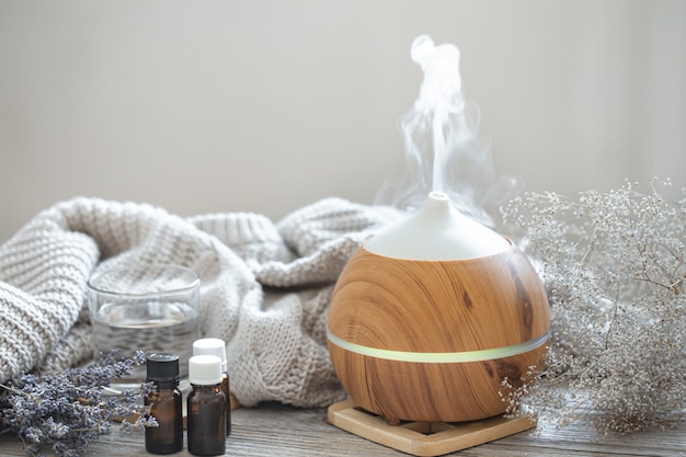 Modern aroma oil diffuser on wood surface with knitted element, water and oils in jars.