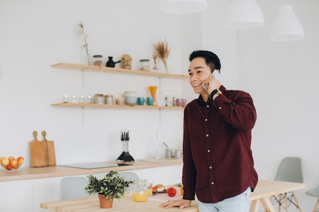 Современный азиатский человек разговаривает по телефону на кухне на завтрак.